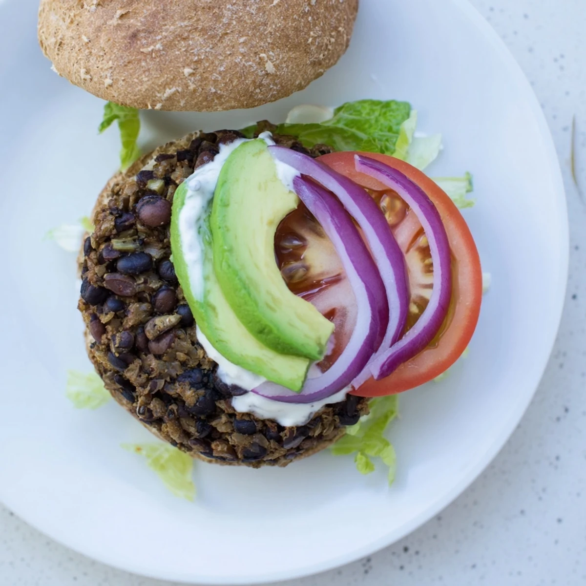 A close-up shot of a juicy zesty black bean burger on a toasted bun with creamy avocado slices.