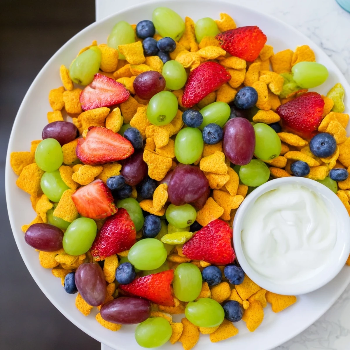 Brightly colored rainbow Goldfish crackers blanketed in berries, ready for dipping in a sweet yogurt sauce.