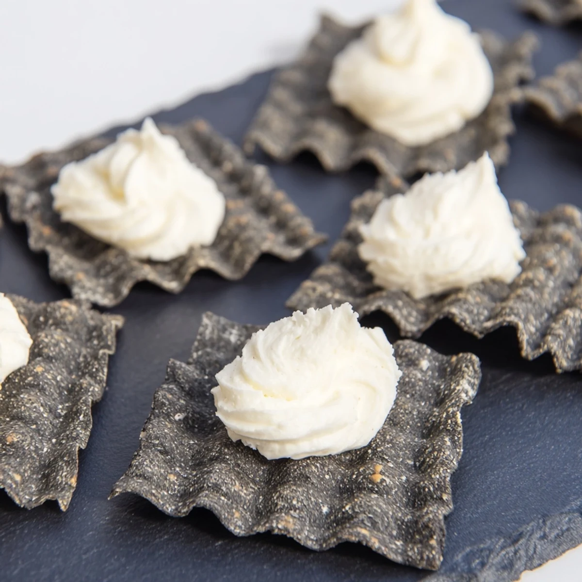 A beautiful display of The Stormy Sea appetizer, highlighting creamy white cheese atop charcoal crackers, ready to eat.
