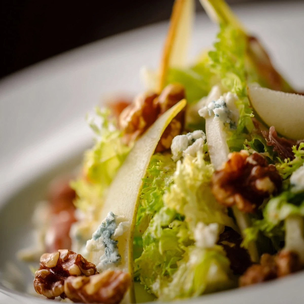 A vibrant plate of Frisée, Pear, Blue Cheese, and Crispy Prosciutto Salad topped with golden prosciutto shards and walnuts.