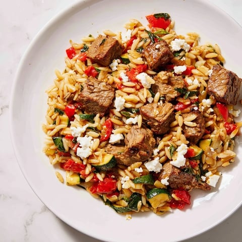 Sizzling Smoky Mediterranean Lamb and Orzo Supper with feta, herbs, and lemon wedges, ready to enjoy.