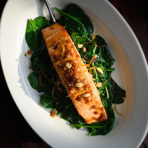 Freshly baked miso salmon on sautéed spinach, garnished with lemon wedges for a bright, savory finish.