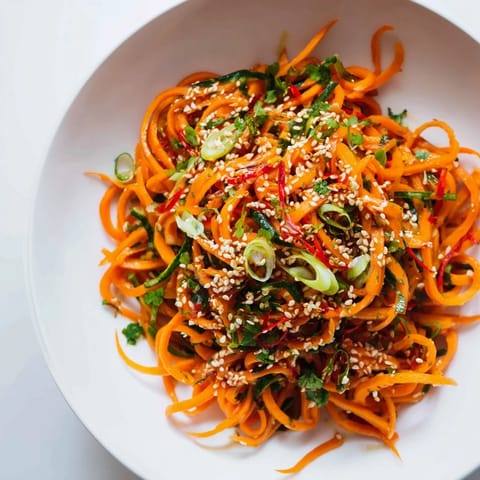 A close-up of the crunchy vegan Carrot Ribbon Salad Asian-Style, featuring bright orange ribbons, sliced green onions, and red chili for a pop of color.