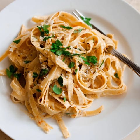 A close-up of Sriracha Honey Pasta reveals glossy noodles coated in a sweet and spicy creamy garlic butter sauce.  