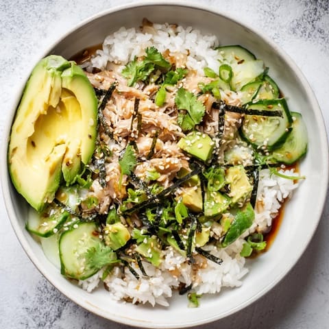Enjoy a colorful Tuna Avocado Rice Bowl featuring crisp cucumber slices and flaky tuna atop fragrant rice, drizzled with a savory sesame ginger dressing.  