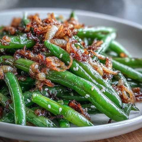 Aromatic sesame garlic green beans with crispy fried onions, showcasing vibrant green vegetables in a savory Asian-inspired side dish.  