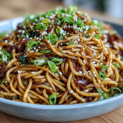 Aromatic Asian ginger scallion noodles with sautéed greens, garnished with sesame seeds and chili for extra flavor.