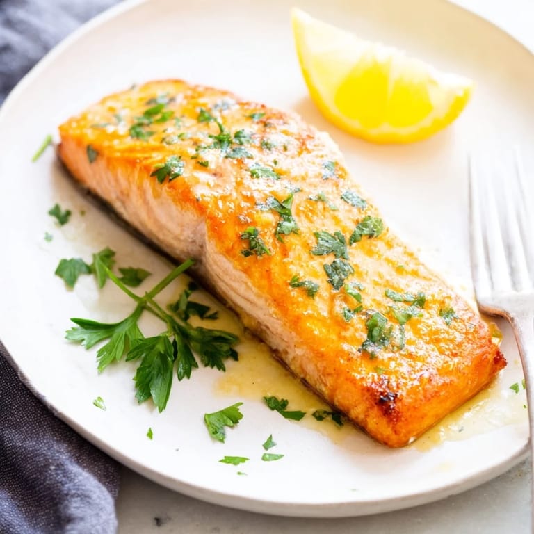 Four servings of Honey Garlic Glazed Salmon resting on a parchment-lined baking tray, ready for a quick and elegant dinner.