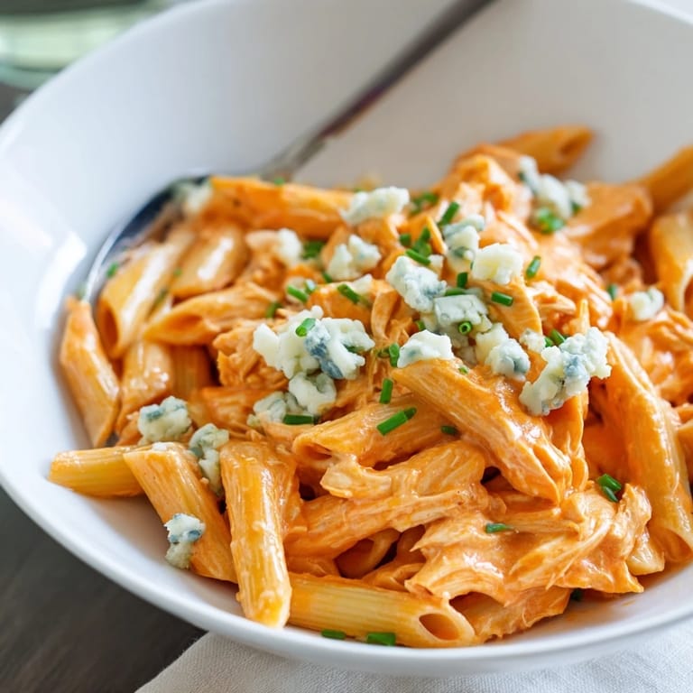 A skillet of Buffalo Chicken Pasta steams beside fresh celery, showcasing rich, velvety sauce and a bold kick.