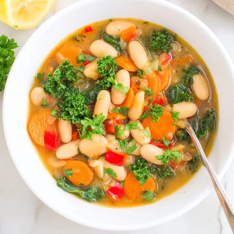 A spoon dipping into a warm Mediterranean White Bean Stew, highlighting the savory broth and vibrant kale and tomatoes.