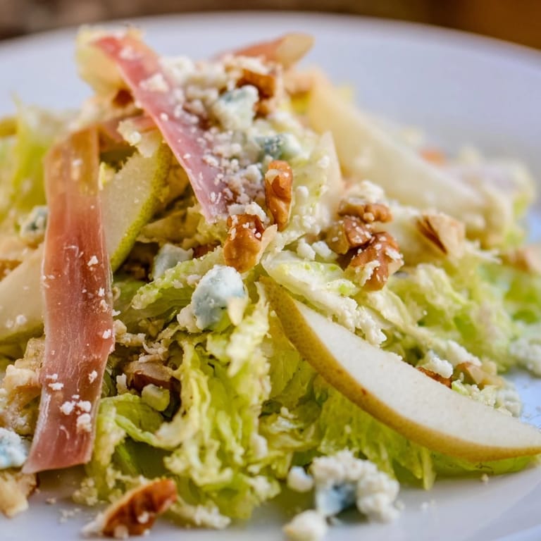 A close look at Frisée, Pear, Blue Cheese, and Crispy Prosciutto Salad showing toasted nuts and a light tangy vinaigrette drizzle.