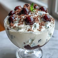 Fluffy Yogurt Berry Sundaes with Dark Chocolate Shavings in clear glass bowls, topped with fresh mint leaves and vibrant mixed berries.