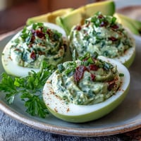 Fresh avocado deviled eggs with vibrant green filling, garnished with herbs and paprika for a healthy spring appetizer.