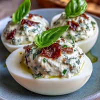 Caprese Deviled Eggs with Basil Oil and Tomato: Creamy yolk filling topped with diced tomatoes, mozzarella, and fresh basil, drizzled with vibrant green basil oil.
